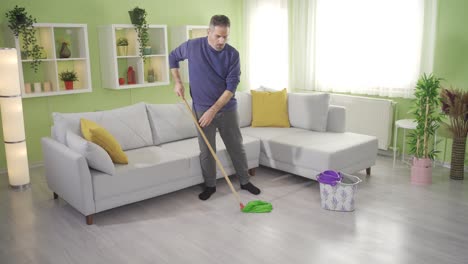 Mature-man-mopping-floor-with-mop-in-living-room-at-home-and-getting-tired.